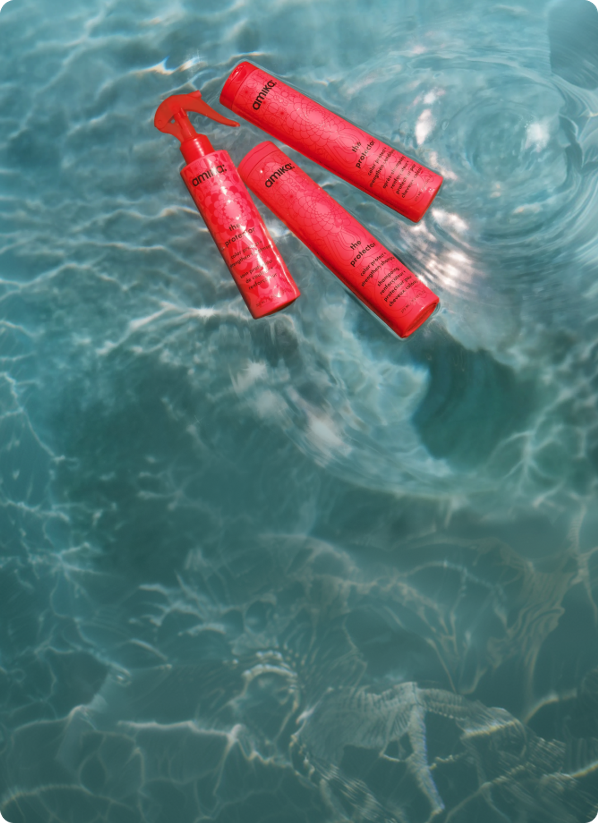 bottles of amika's the protector shampoo, conditioner, and treatment float in a swimming pool