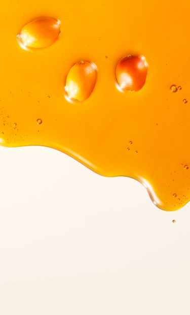 Image of sea buckthorn berries floating within a drop of sea buckthorn oil against a cream background.