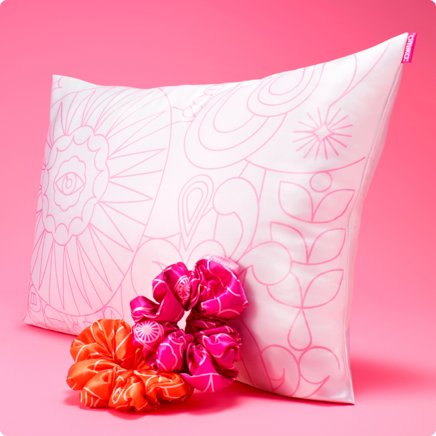 amika pillowcase + scrunchies gift set with purchase - pillow leaning against a pink background with scrunchies in the foreground.