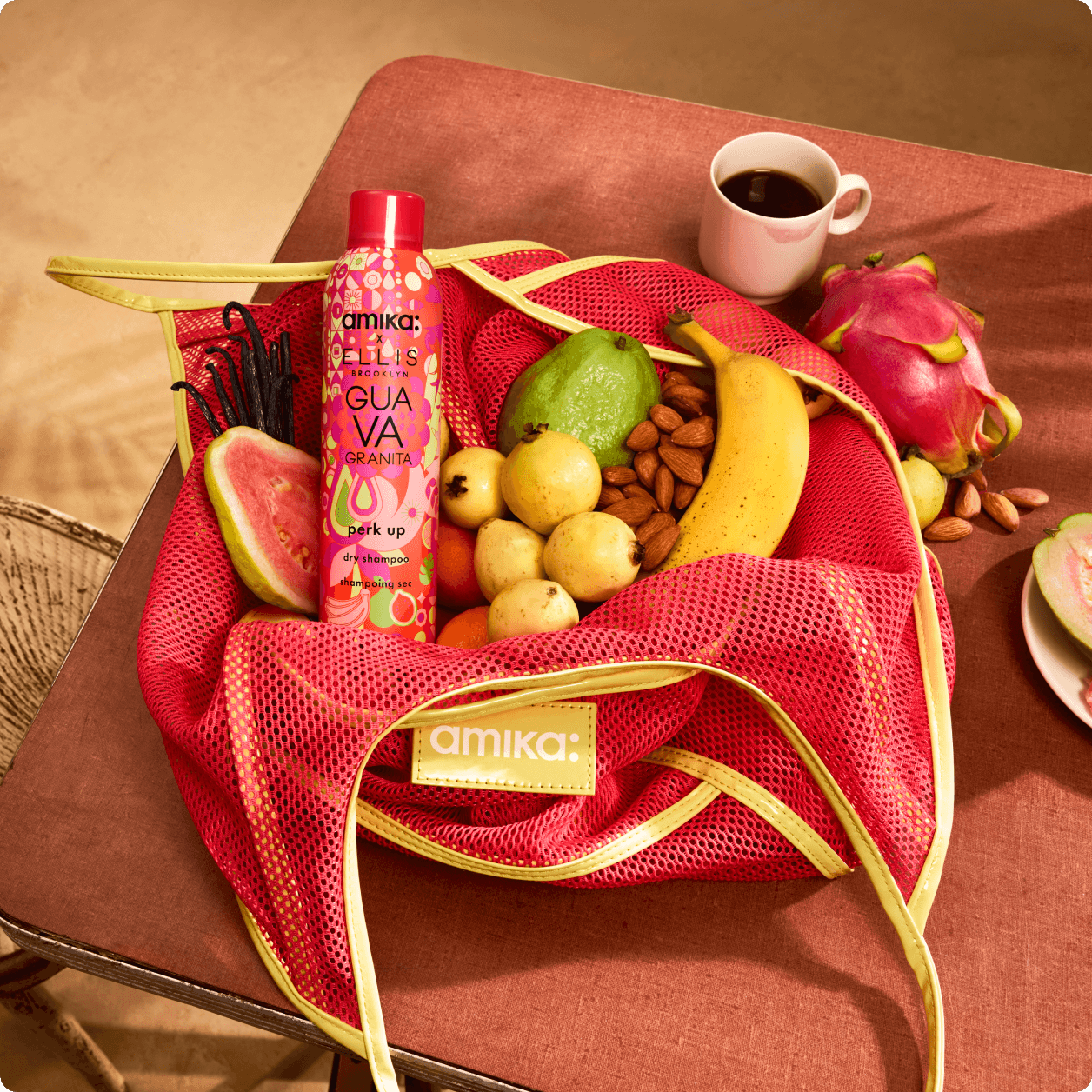 a bottle of amika perk up GUAVA GRANITA sits in a pink mesh bag with guavas, bananas, and vanilla on a table