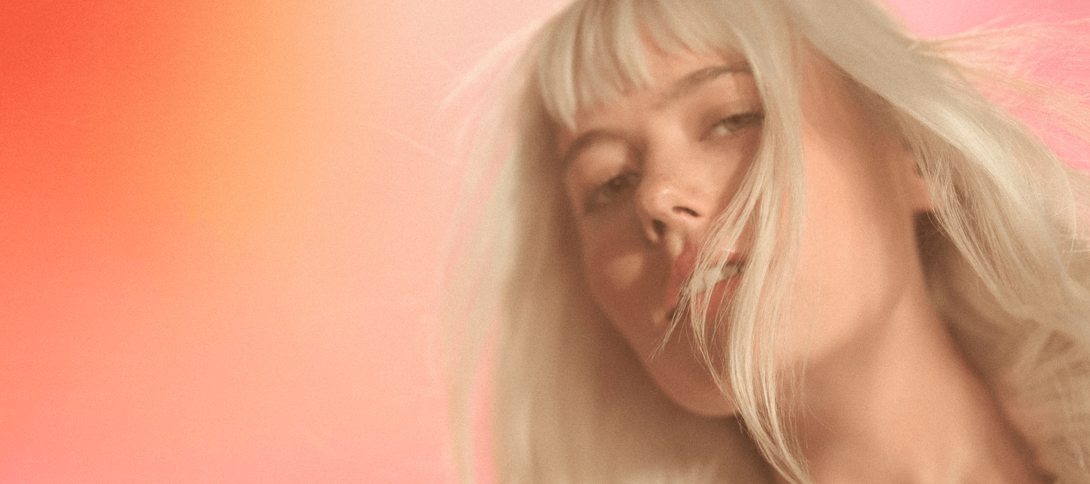 amika model with blonde, straight hair in front of an orange pink gradient background.