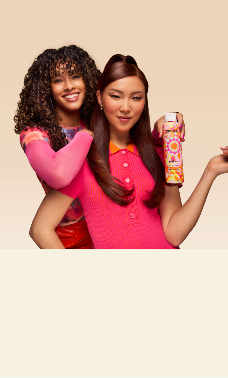 two models pose in front of a cream backdrop. one model holds a bottle of amika perk up dry shampoo