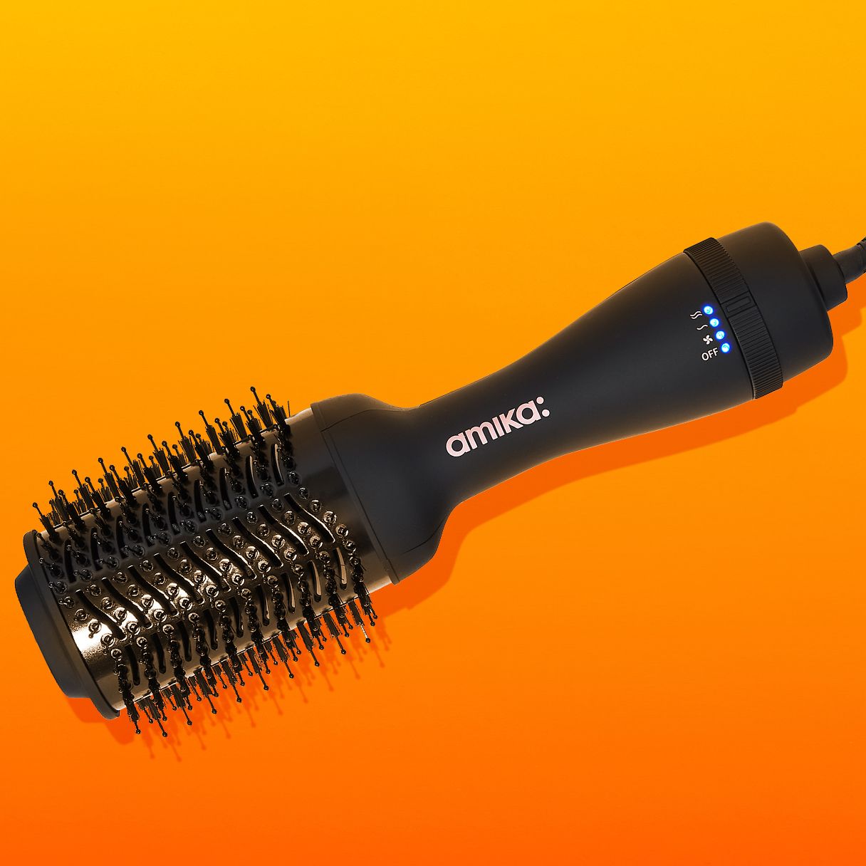 amika hair blow dryer brush 2.0 on an orange and yellow background