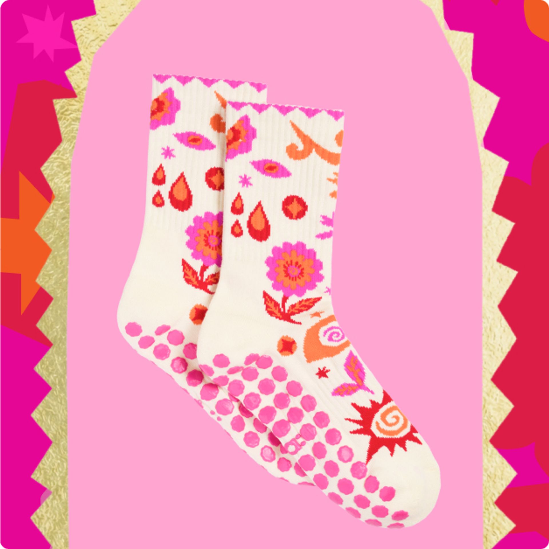 a pair of patterned socks with pink grips on the bottom against a pink background with a gold, red, dark pink, and orange patterned frame.