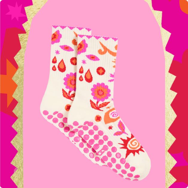 a pair of patterned socks with pink grips on the bottom against a pink background with a gold, red, dark pink, and orange patterned frame.