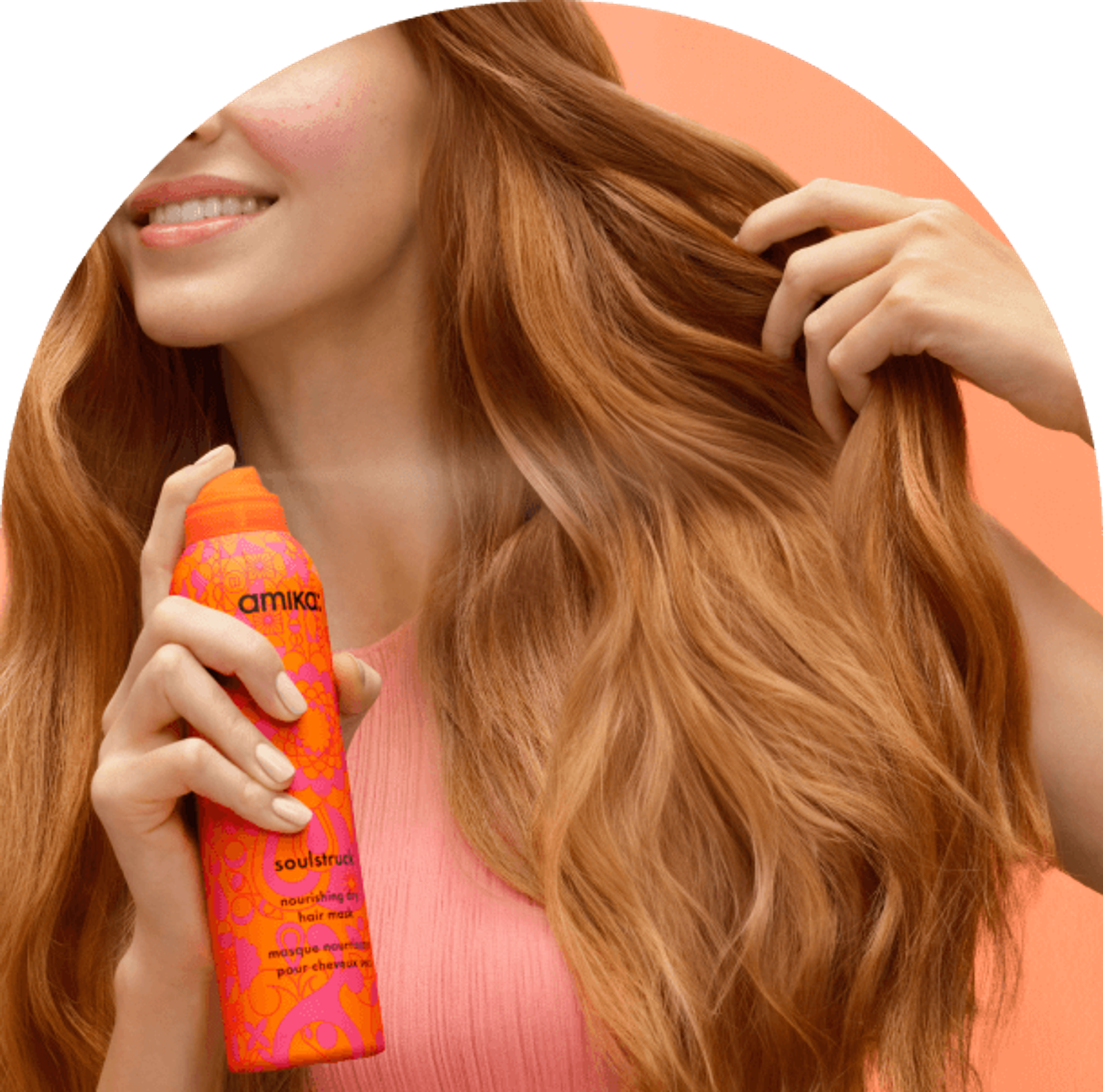 model spraying amika soulstruck dry mask in their hiar in front of a pinkish-orange background