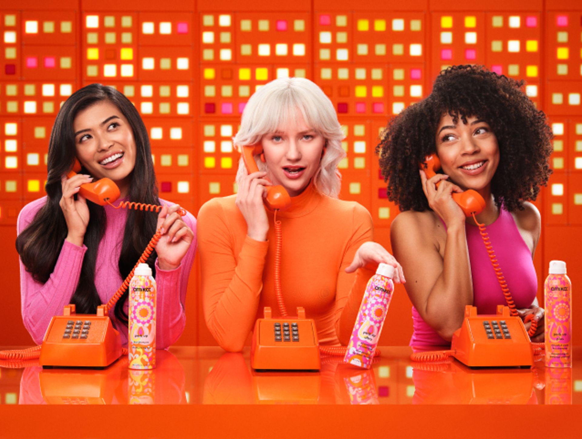 3 models talk on telephones and display amika perk up talc-free dry shampoo, perk up ultra oil control dry shampoo, and perk up plus extended clean dry shampoo.