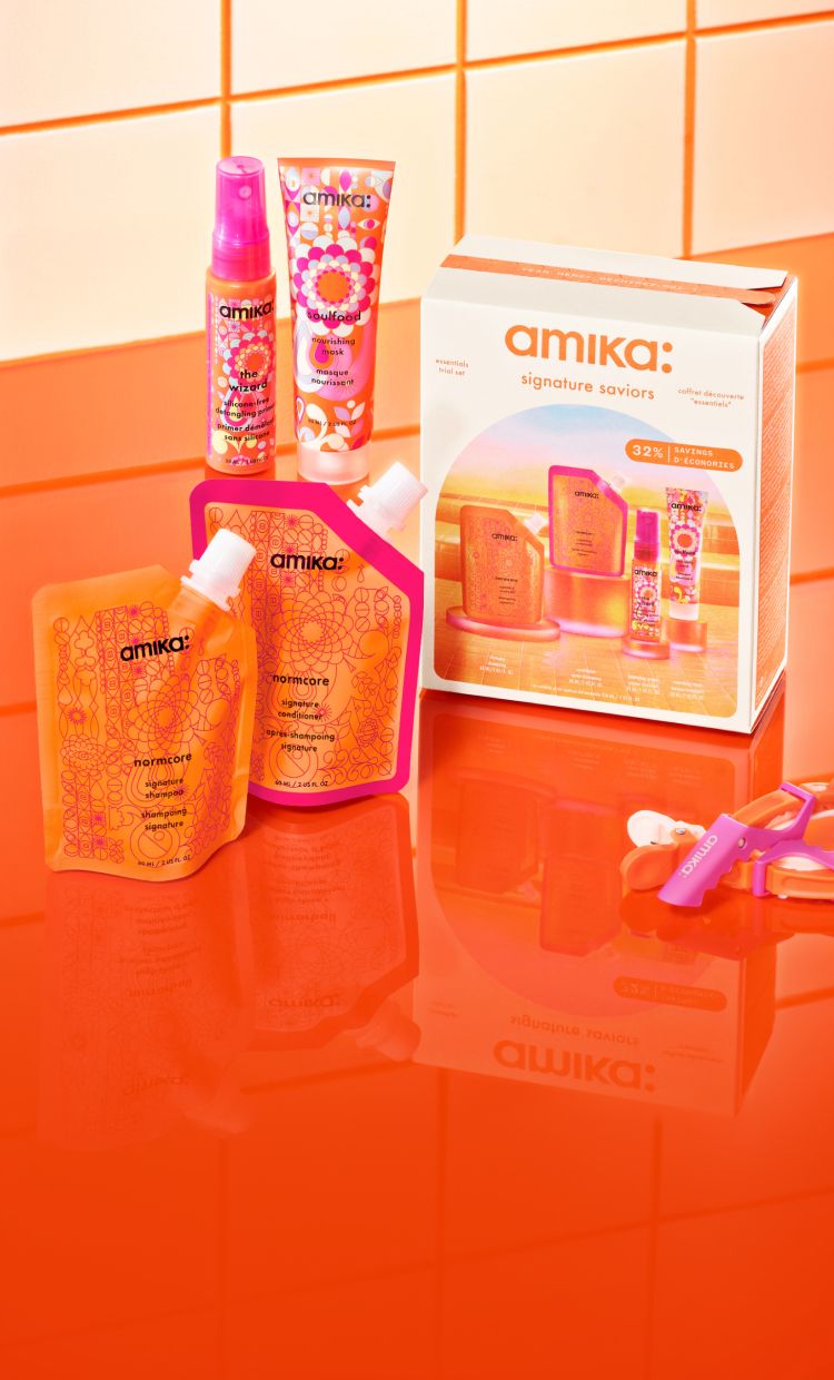 the amika signature saviors set including normcore shampoo and conditioner travel size, the wizard detangling primer travel size and soulfood nourishing mask travel size sitting on top of an orange countertop in front of white/cream tile