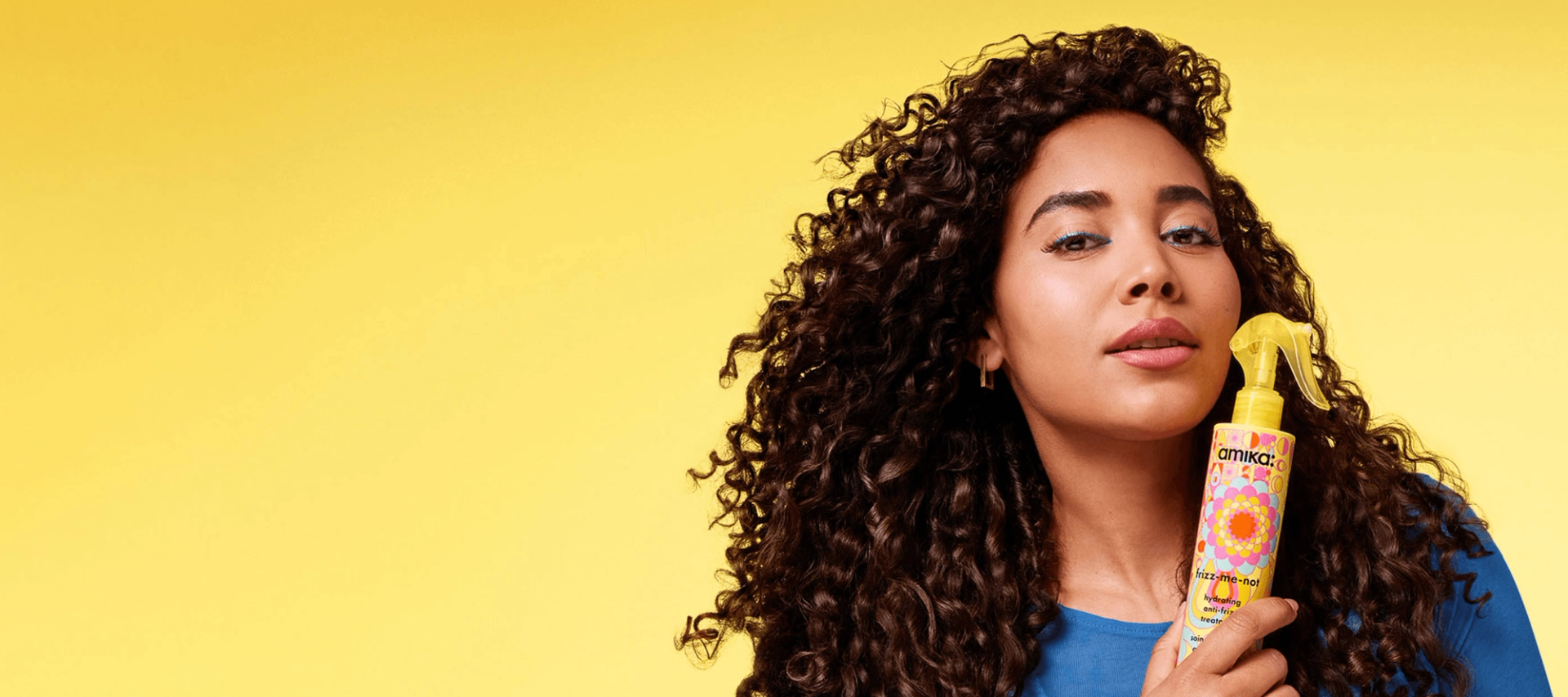 a model holds a bottle of amika frizz-me-not treatment against a yellow background.