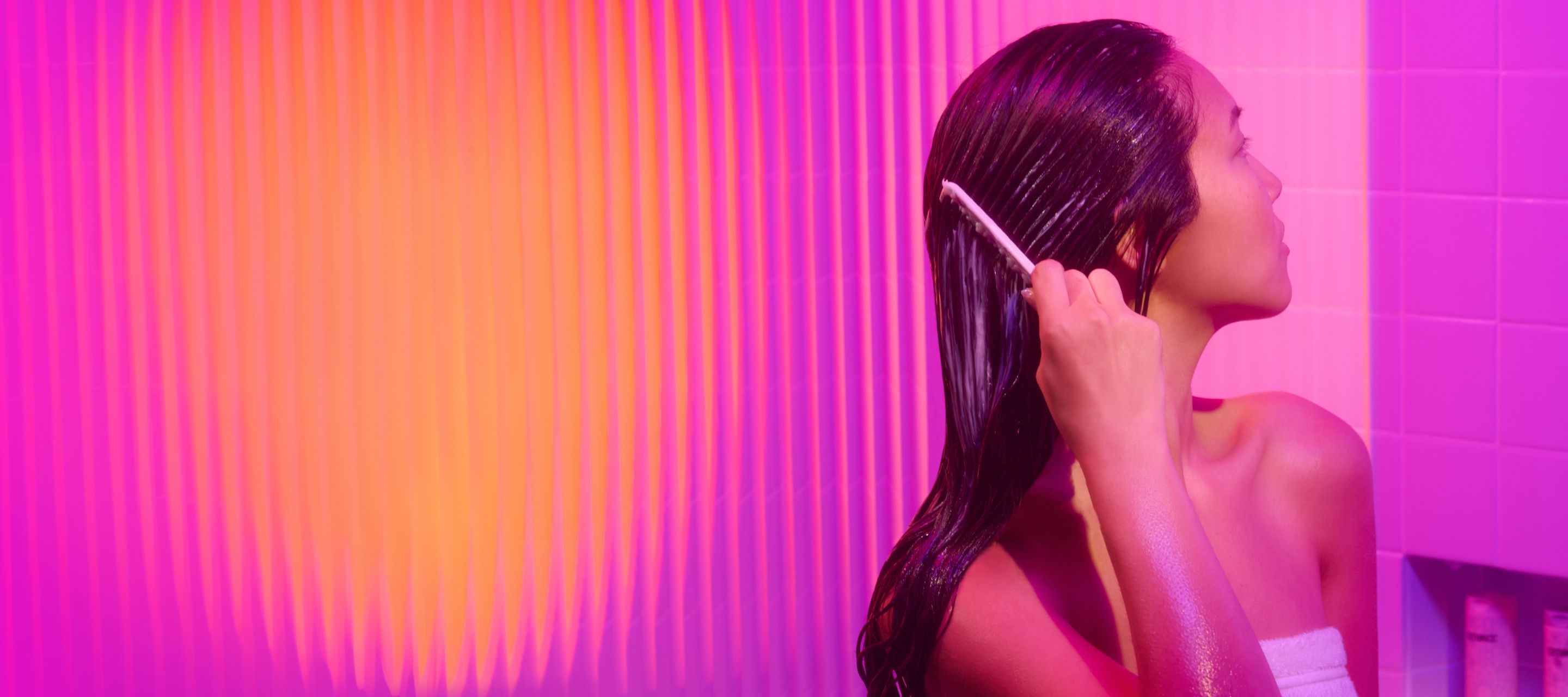 amika model combing through her hair with conditioner suds in her brunette colored hair in front of a purple hued background