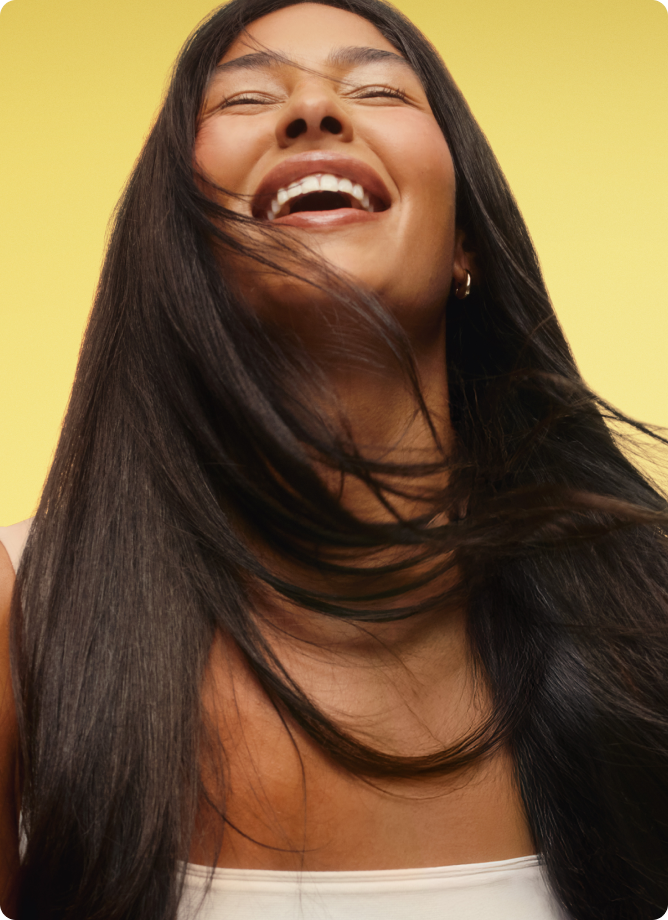 a model with smooth, dark hair smiles posing against a yellow background