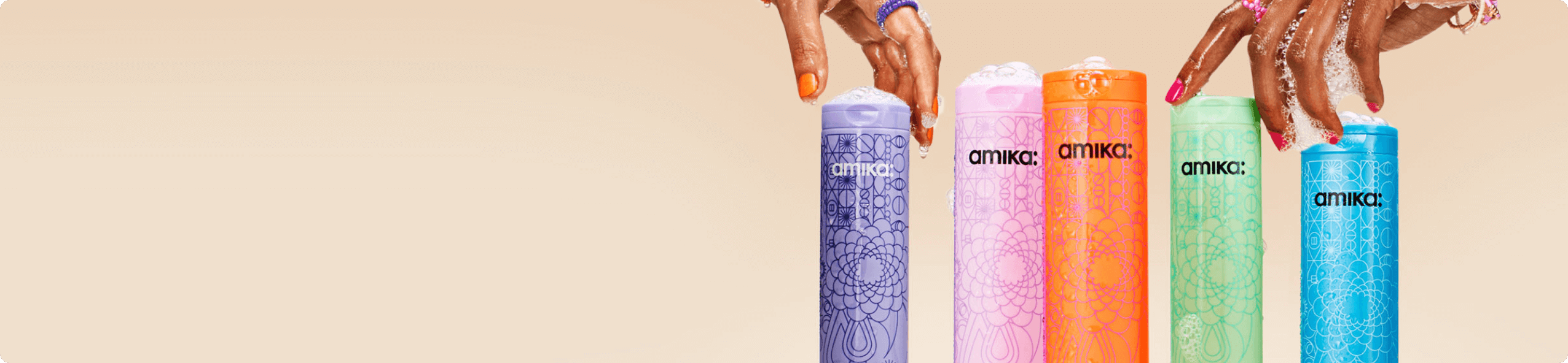 two hands with soapy lather on them reach for amika shampoo bottles against a cream background