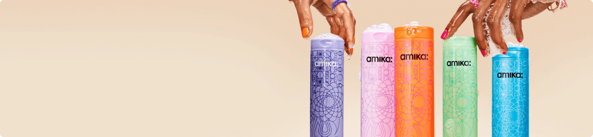 two hands with soapy lather on them reach for amika shampoo bottles against a cream background