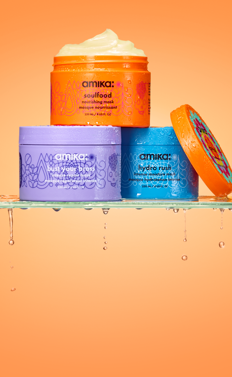 amika masks: hydro rush, soulfood, and bust your brass sit on a wet glass surface in front of an orange background