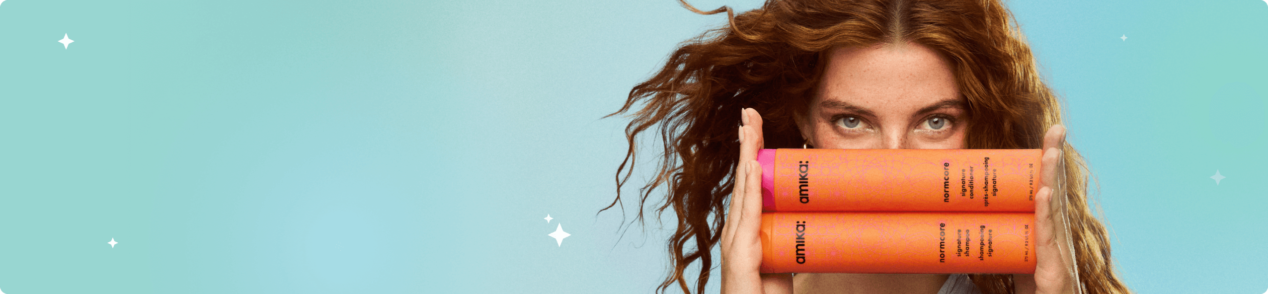 a model holds amika normcore shampoo and conditioner bottles horizontally while against a bluish background