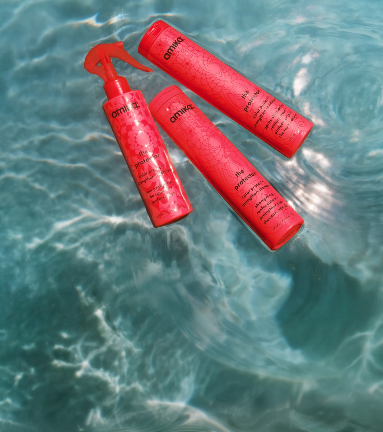 bottles of amika's the protector shampoo, conditioner, and treatment float in a swimming pool