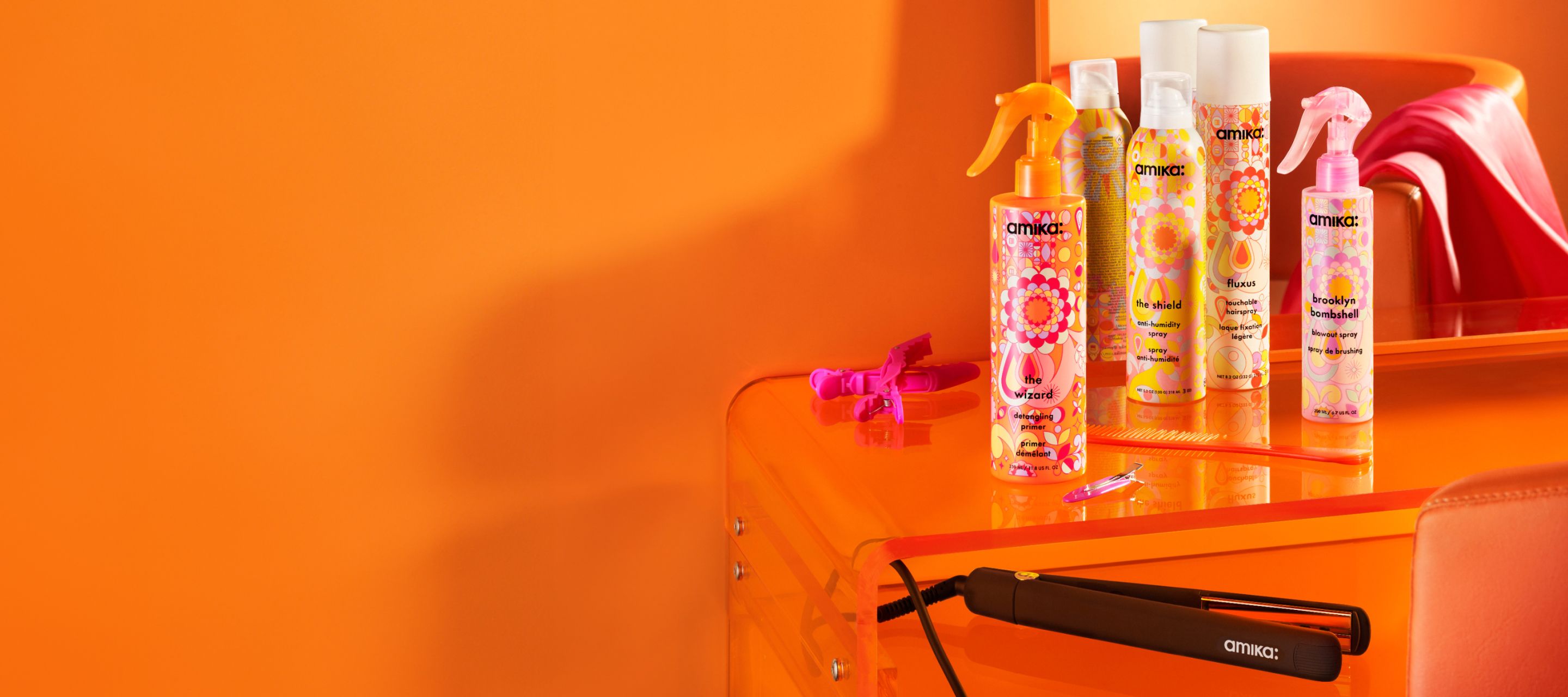 amika hair straightener, the wizard detangling primer, the shield, fluxus and brooklyn bombshell spray on an orange table