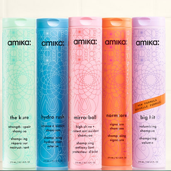 amika bottles of shampoo sit against a white tiled background