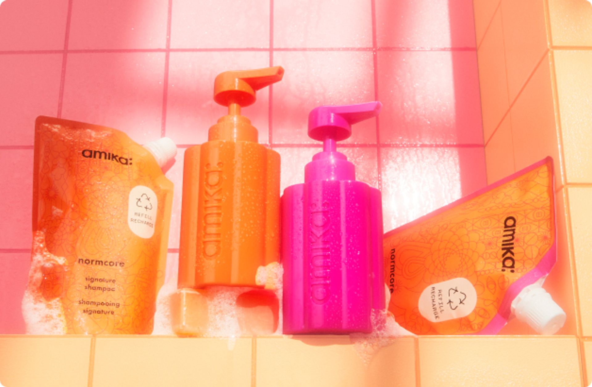 amika normcore shampoo and conditioner 500ml refill pouches with the forever friend refillable bottles on a pink and orange tile background