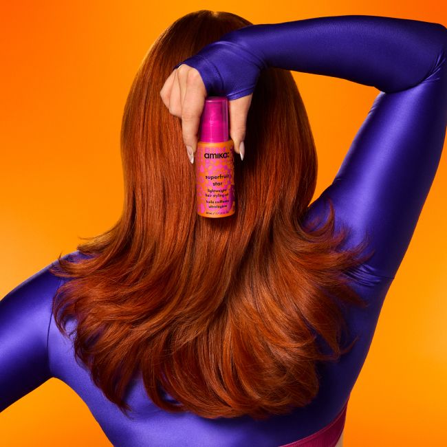 image shows a model holding a bottle of amika superfruit star oil behind their head.