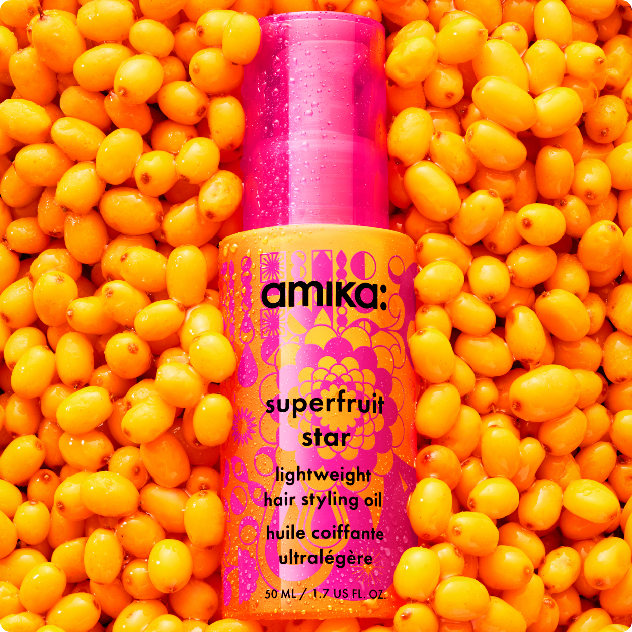 a pink and orange bottle of amika superfruit star lightweight hair styling oil lays on a bed of sea buckthorn berries