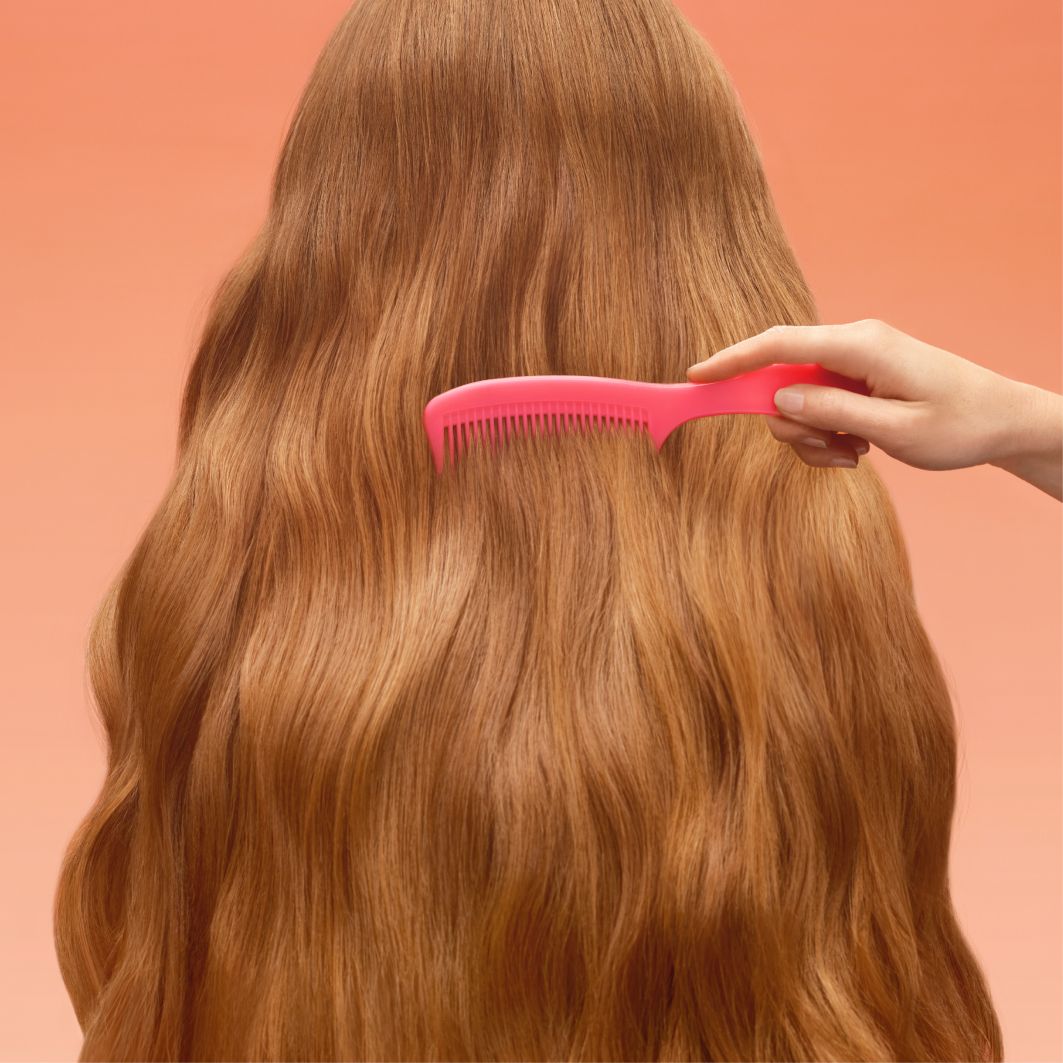 a pink comb moves through reddish hair against a pinkish-orange background