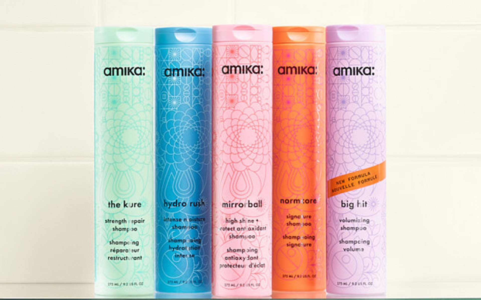 amika bottles of shampoo sit against a white tiled background