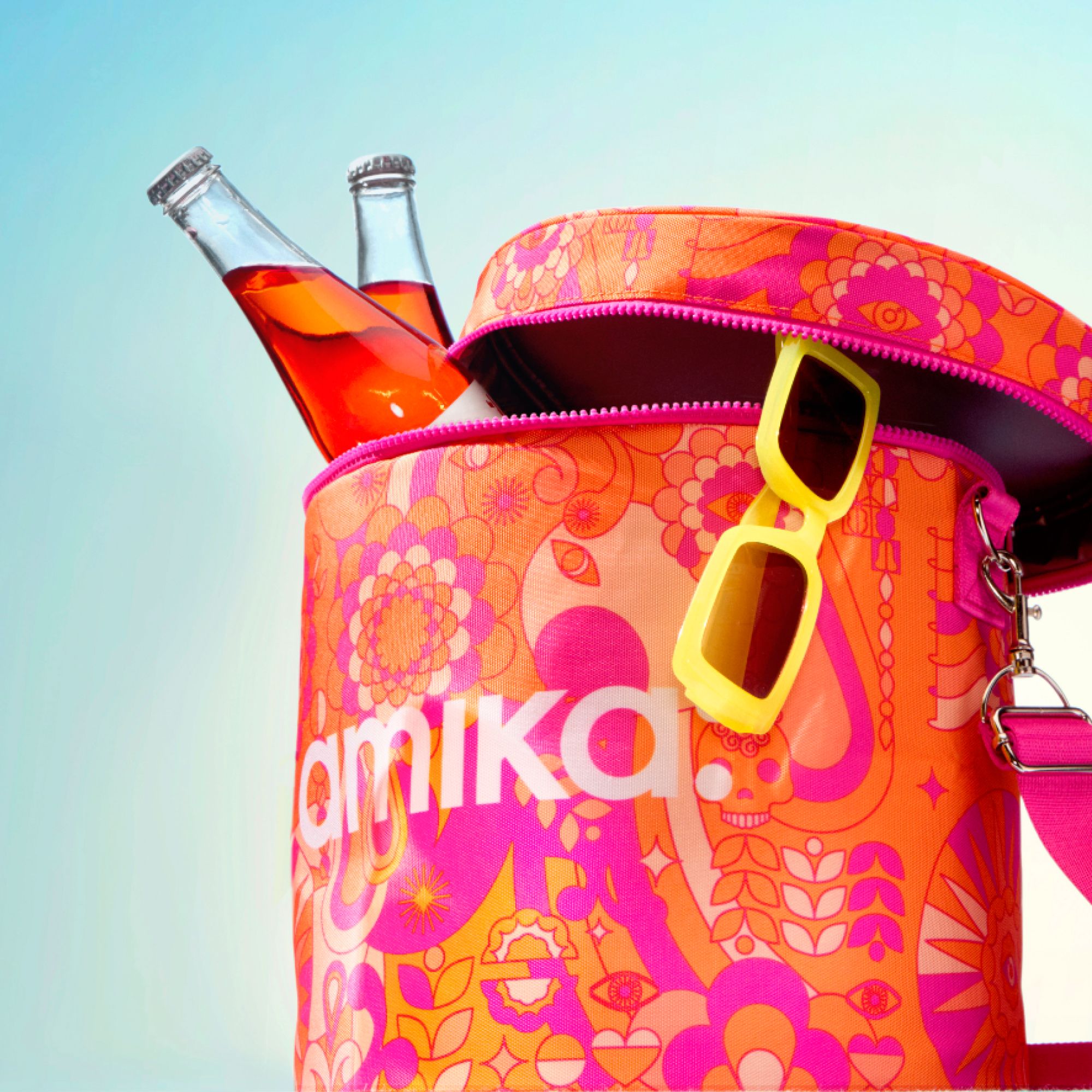 an image of a circular amika bag with yellow sunglasses hanging on the right side and two glass bottles of beverage inside the bag on the left side