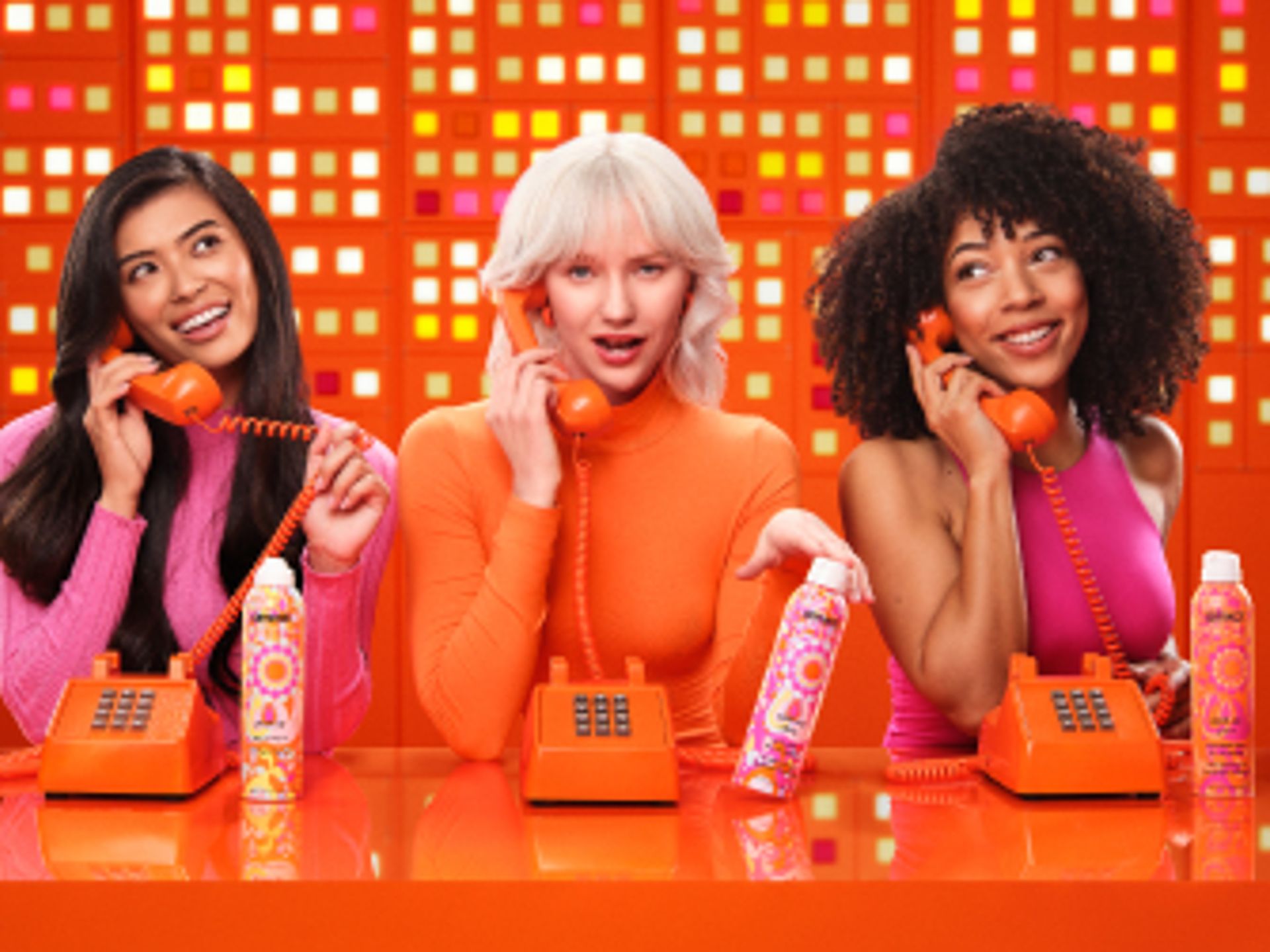 3 models talk on telephones and display amika perk up talc-free dry shampoo, perk up ultra oil control dry shampoo, and perk up plus extended clean dry shampoo.