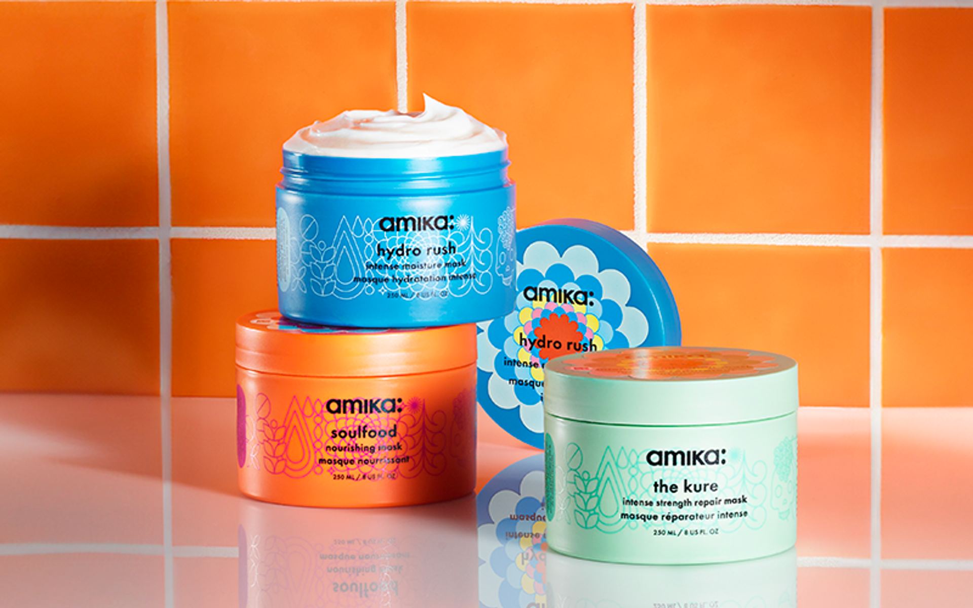 amika masks: hydro rush, soulfood, and the kure sit on a shiny white surface in front of an orange tiled background
