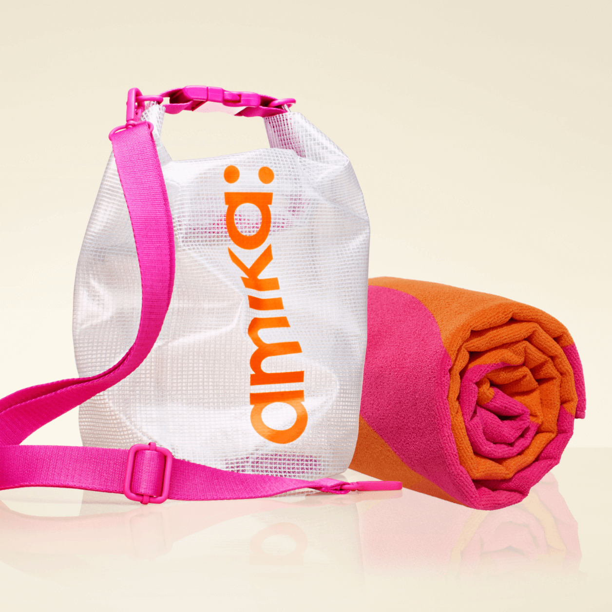 amika beach-ready bundle: an orange and pink towel rolled up next to a clear dry bag with pink strap and amika: logo in orange
