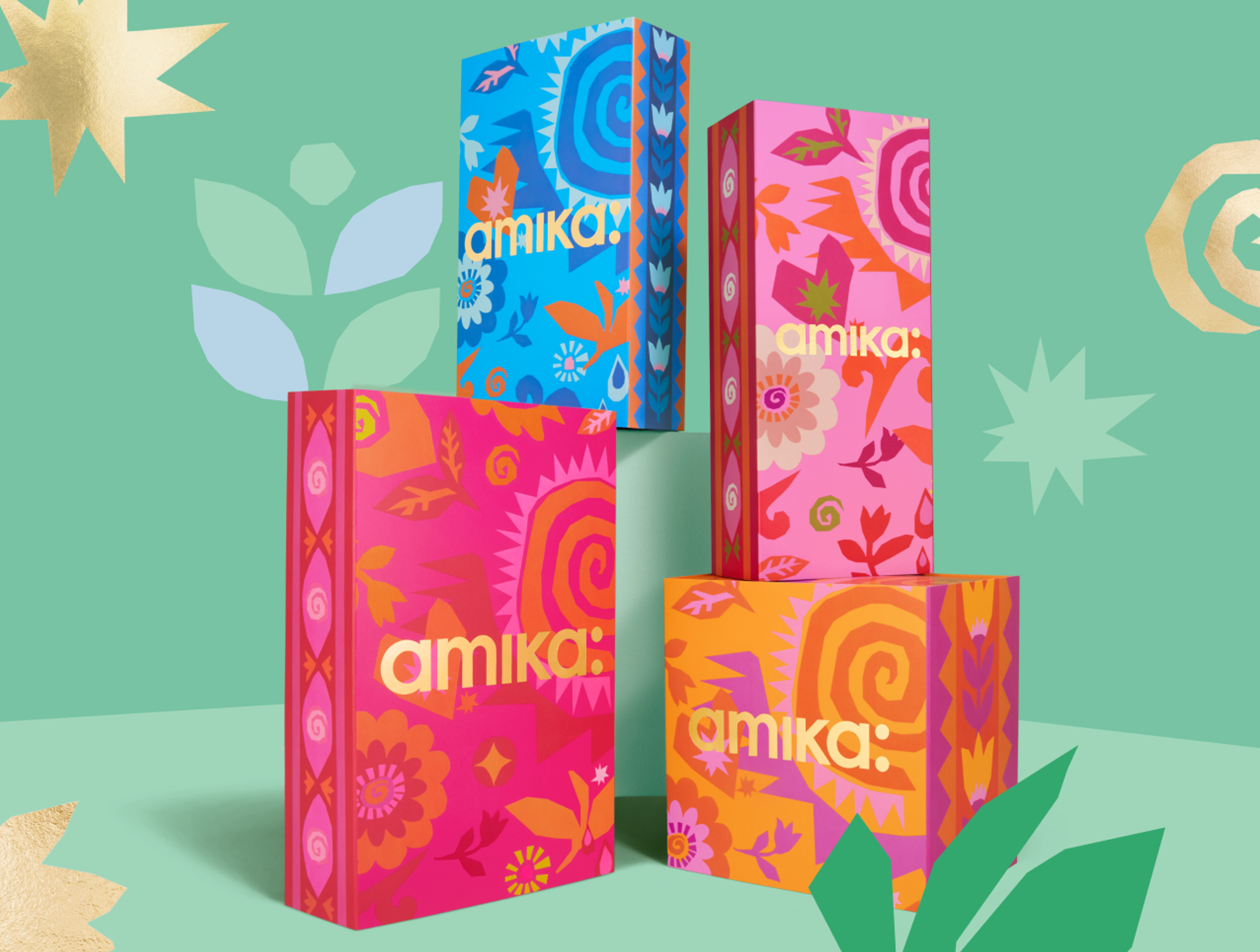 four amika gift set boxes arranged against a light green and darker green patterned background