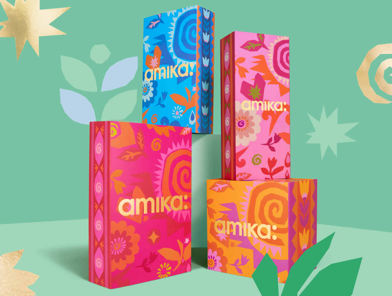 four amika gift set boxes arranged against a light green and darker green patterned background