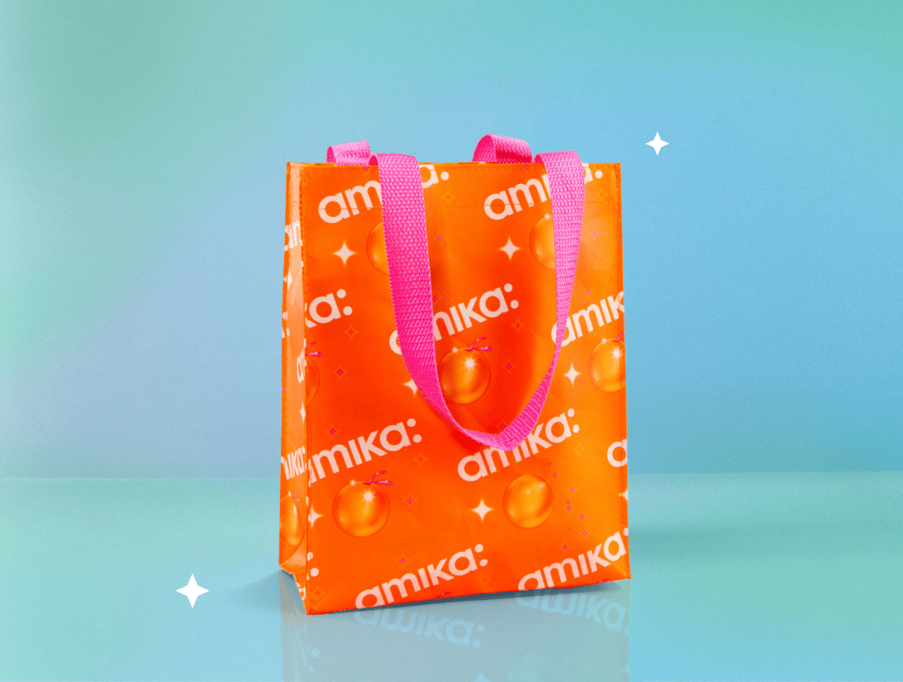 an orange tote bag with pink handles that features a white amika logo and large sea buckthorn berries sits against a light blue background