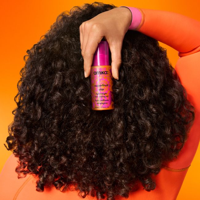 image shows a model holding a bottle of amika superfruit star oil behind their head.