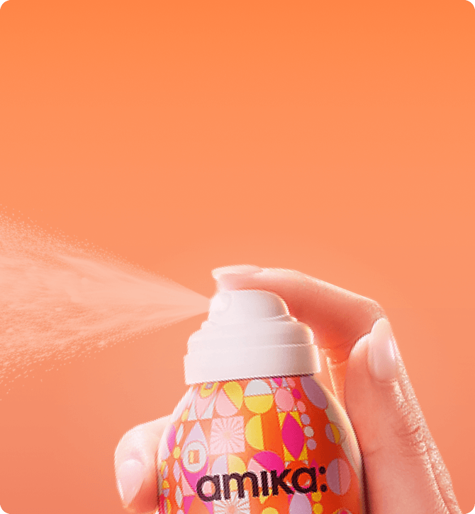 a bottle of amika dry shampoo spraying against an orange background