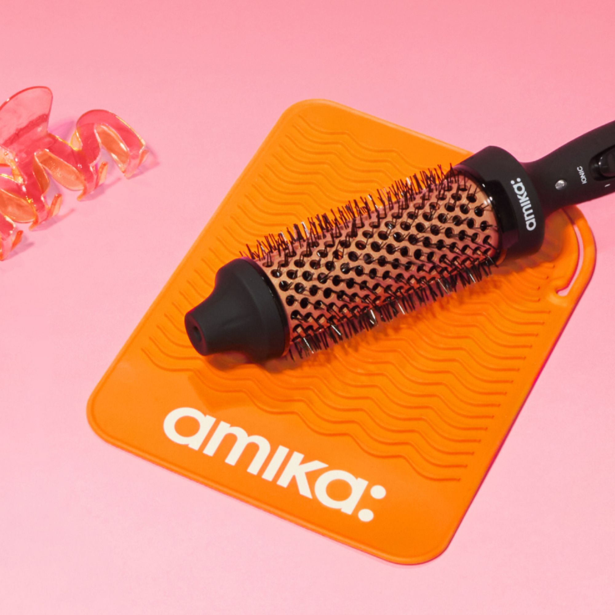 an amika blowout babe thermal brush lies on top of an orange amika heat mat for tools