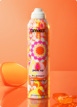 a bottle of amika perk up dry shampoo against an orange background