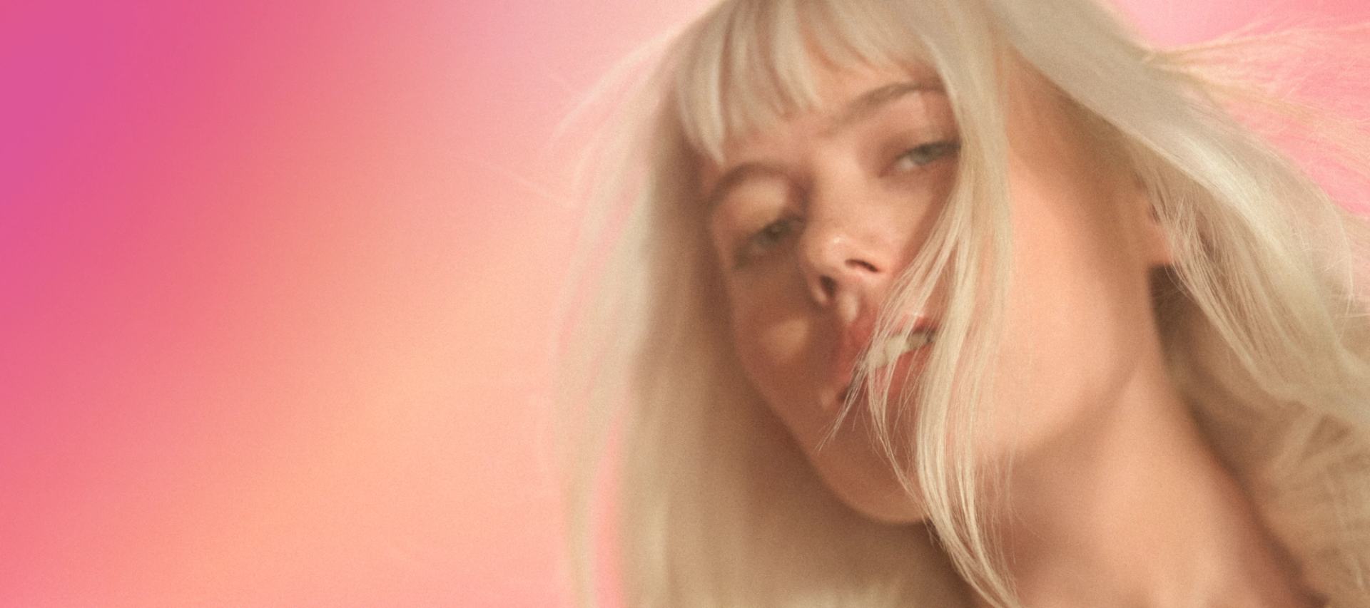 a model with their hair flowing stands against a pink and orange gradient background