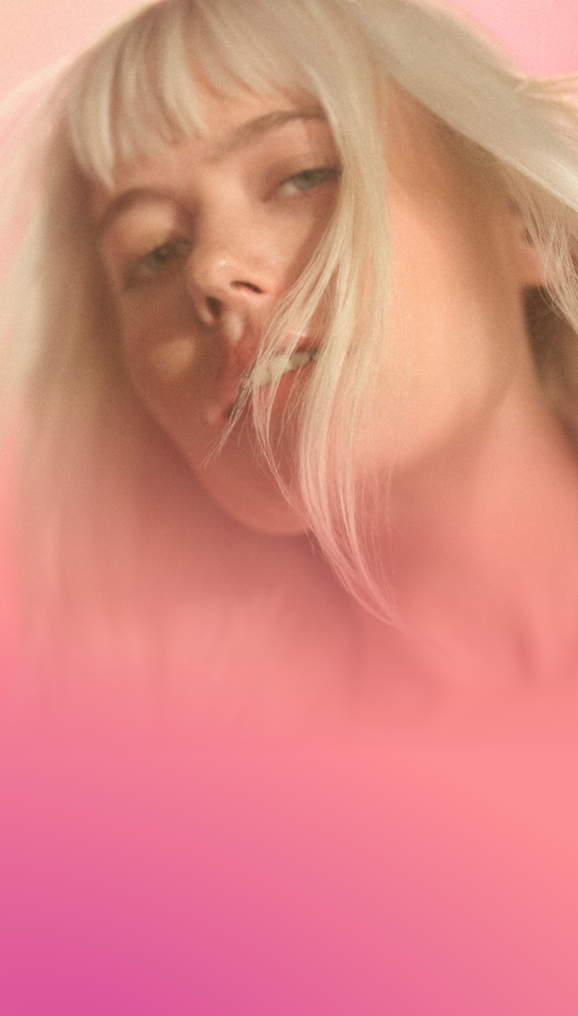 a model with their hair flowing stands against a pink and orange gradient background