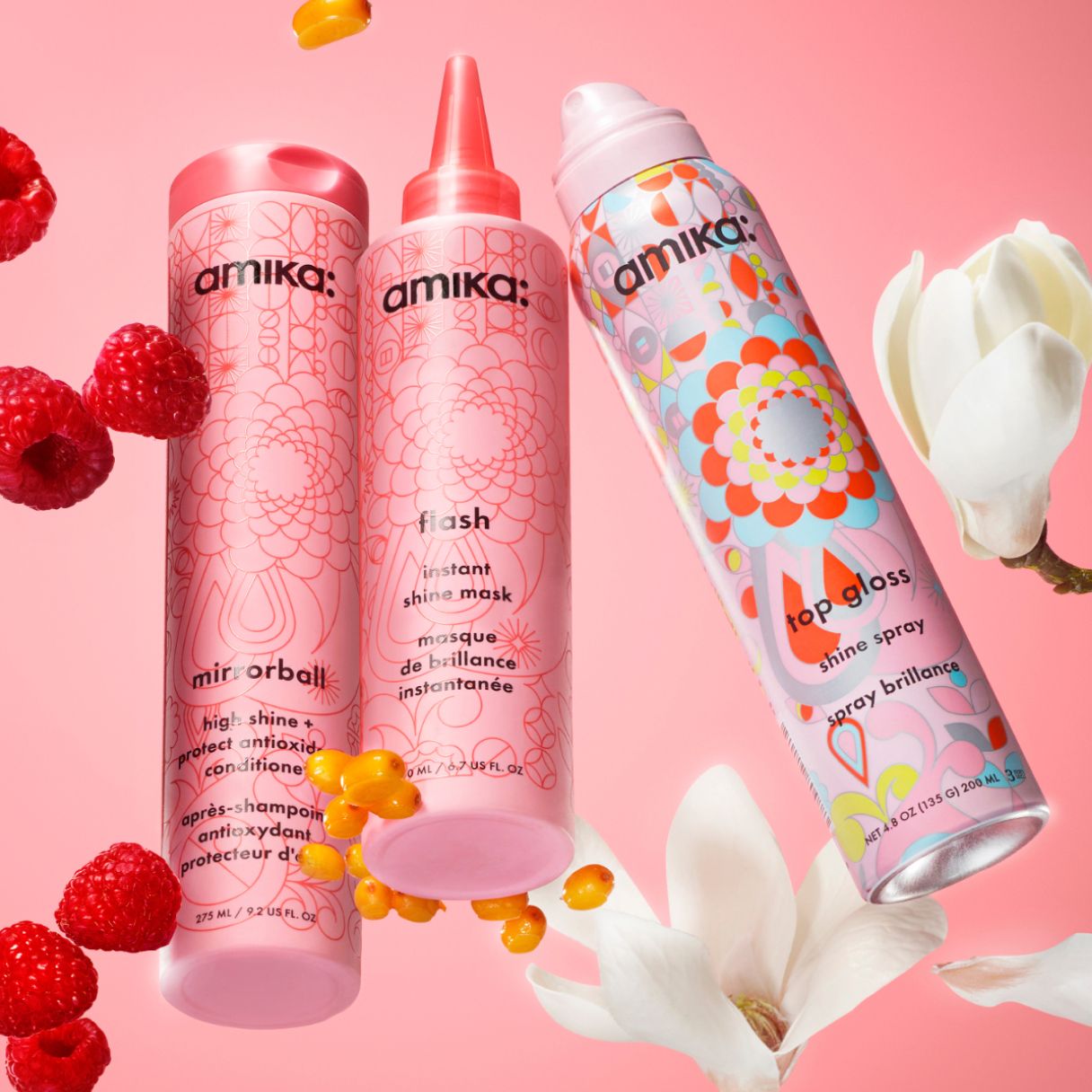 amika mirrorball conditioner, flash instant shine mask and top gloss shine spray on a pink background surrounded by raspberries and white flowers