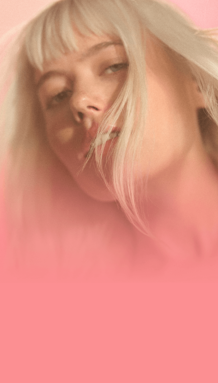 amika model with blonde, straight hair in front of an orange pink gradient background.