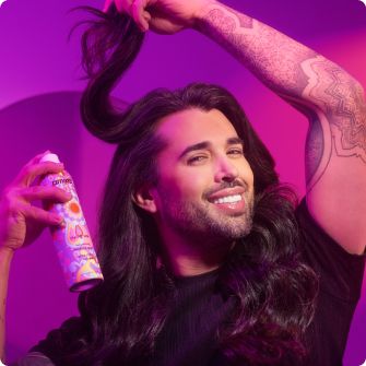 photo of a guy with long wavy hair holding his hair with left arm spraying the rising star spray into his root
