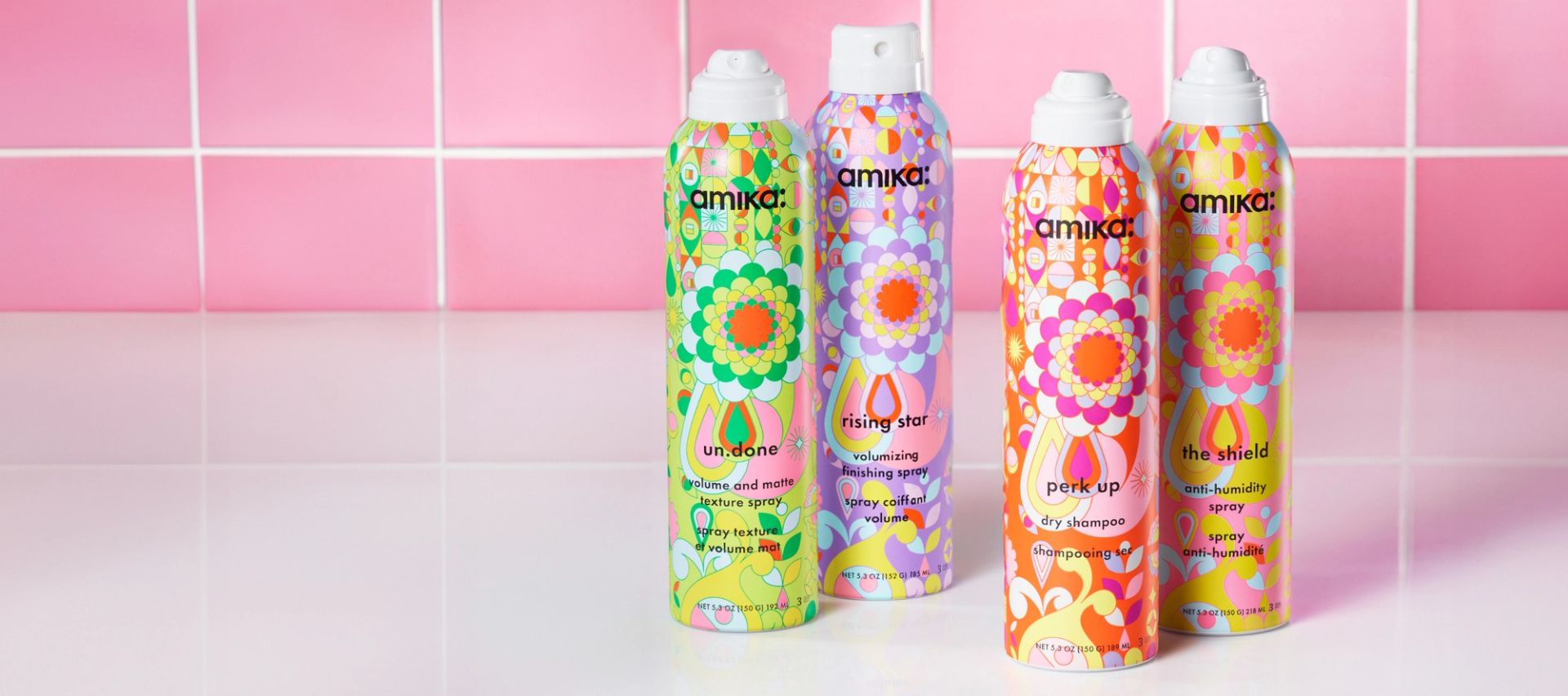 amika un.done volume and matter texture spray, rising star volumizing finishing spray, perk up dry shampoo and the shield ant-humidity spray full size products sitting in front of a white sink with a pink tile background