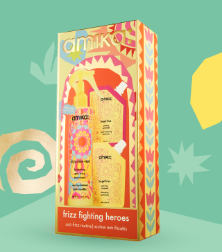 amika frizz fighting heroes holiday gift set posed against a light green background and with some gold shapes behind the box