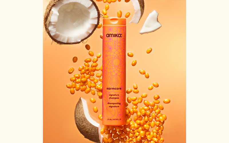 amika normcore signature shampoo surrounded by seabuckthorn and coconut ingredients on an orange background