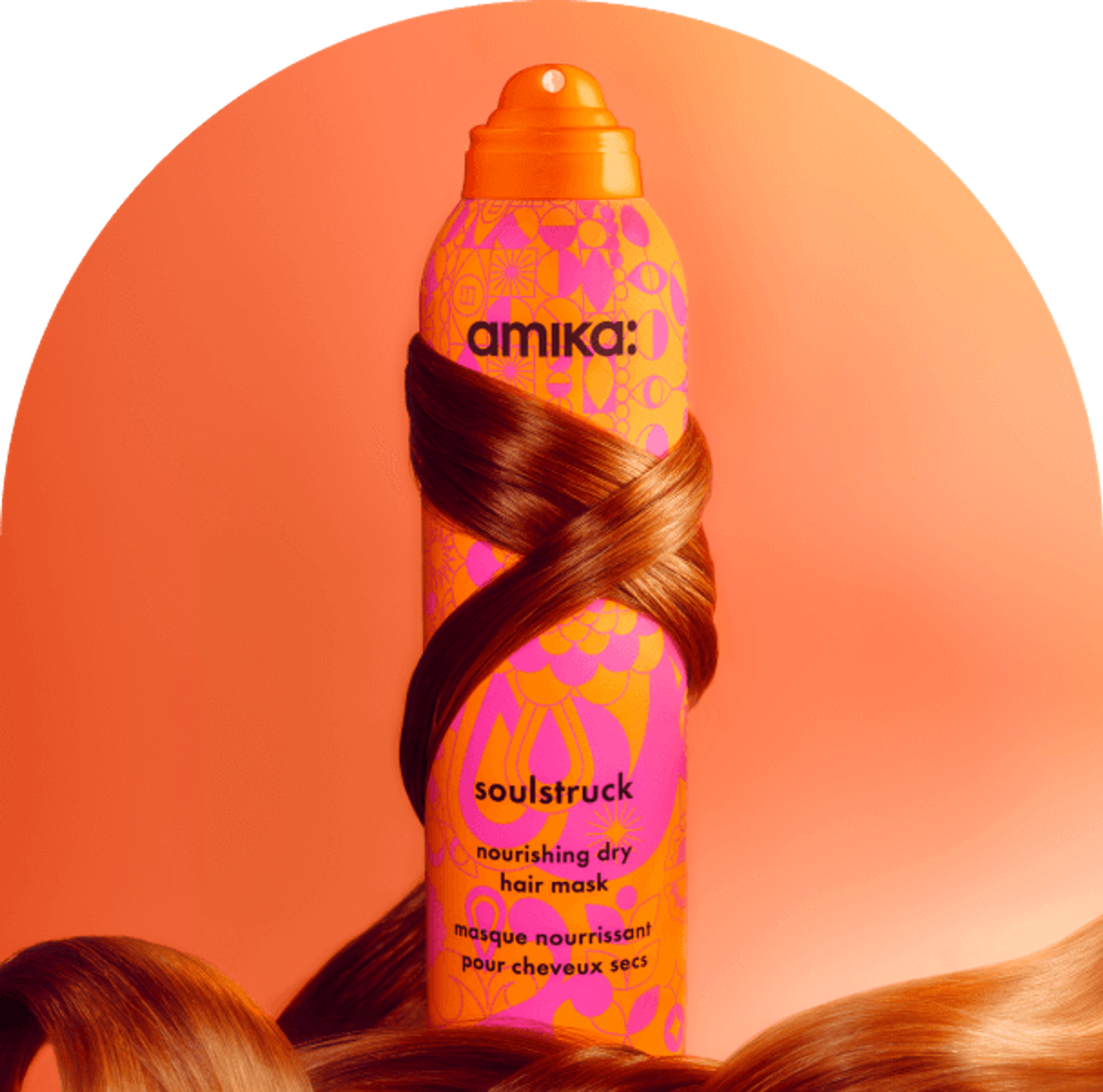 a tress of reddish brown hair wraps around amika soulstruck spray. the bottle sits in front of a pinkish-orange background