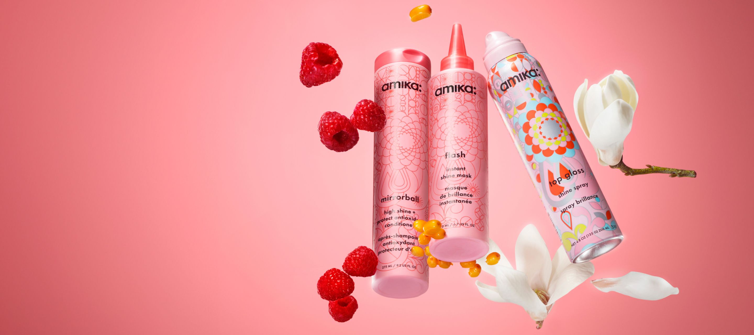 amika mirrorball conditioner, flash instant shine mask and top gloss shine spray on a pink background surrounded by raspberries and white flowers