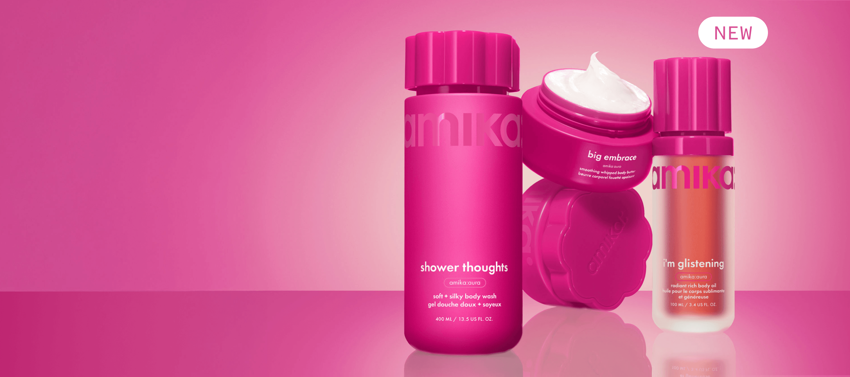 amika shower thoughts body wash, i'm glistening body oil, and big embrace body butter sit against a pink gradient background