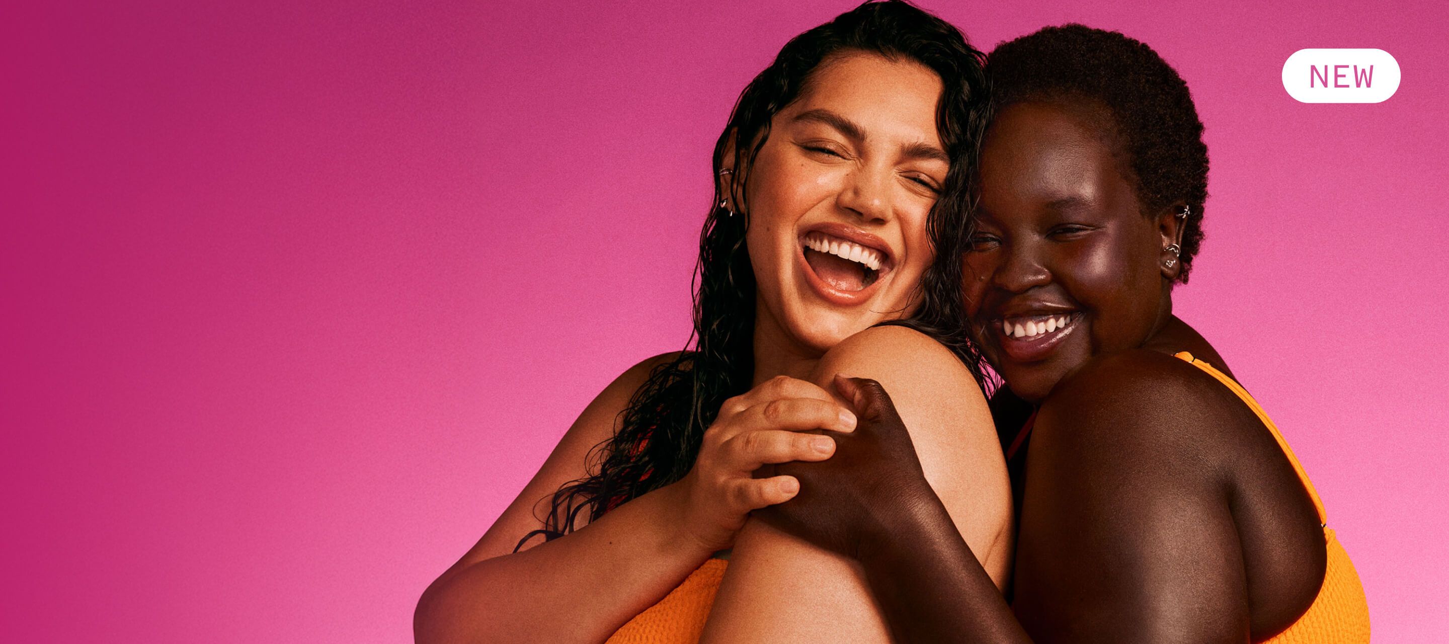 two models embrace with glowing skin in front of a pink background